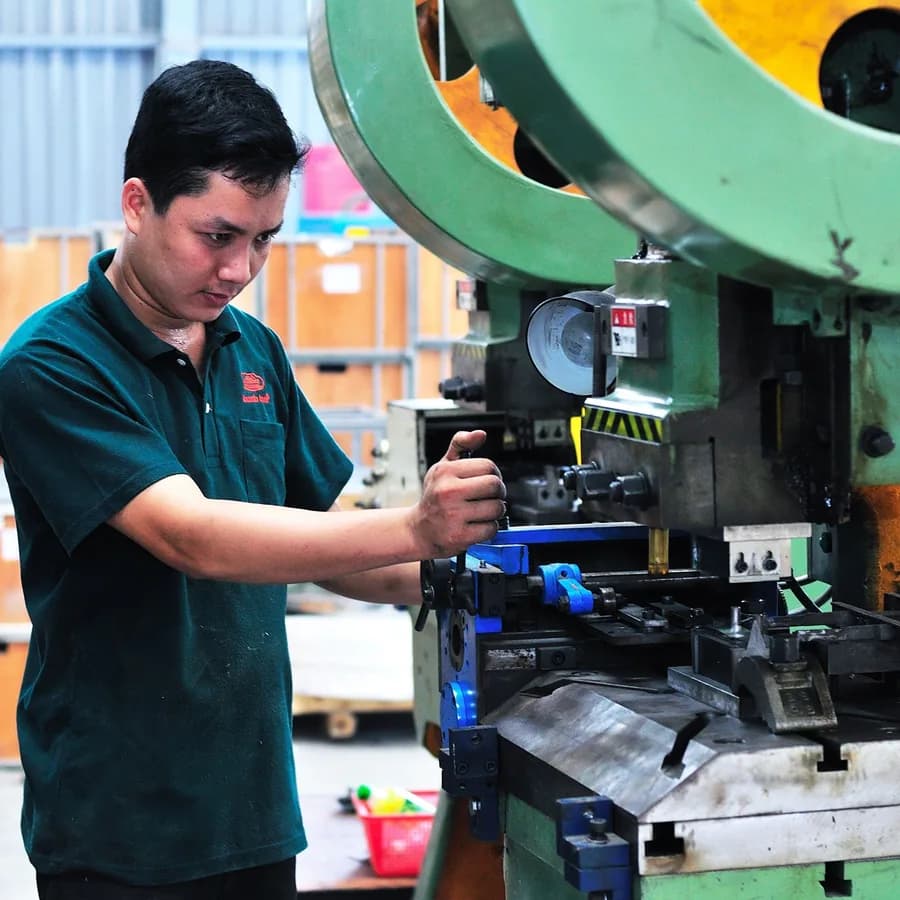 A machine operator setting up an industrial press on a factory floor