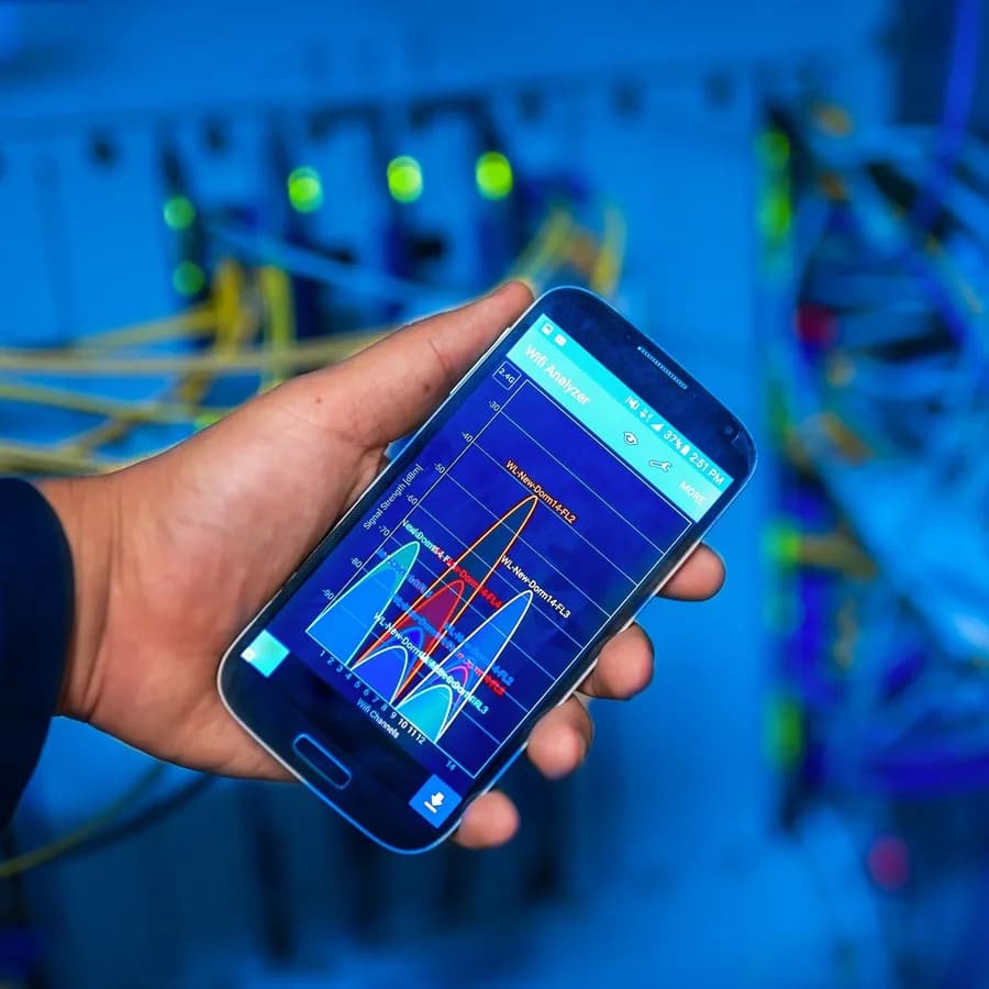 A technician checking network signal readings on a phone beside a fibre-optic patch panel